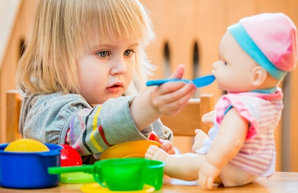 A child feeding a baby doll with a spoon