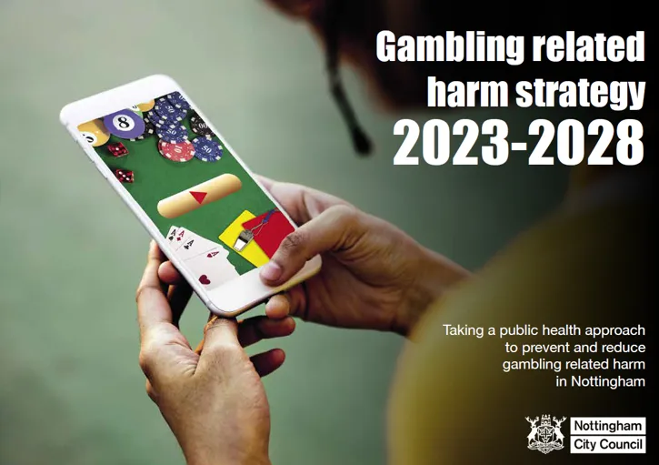 Person holding a smartphone displaying a gambling game, with text about a gambling harm strategy for 2023-2028 from Nottingham City Council.