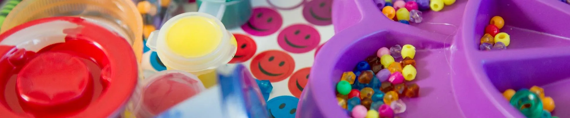 Colorful art supplies including paint, brushes, and beads organized in various containers on a table.