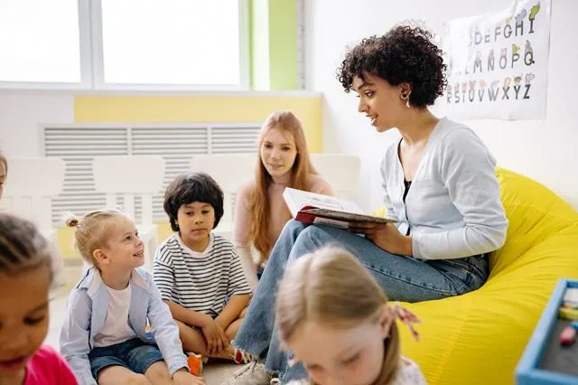 A childminder sitting on a bean sack reading to young children.