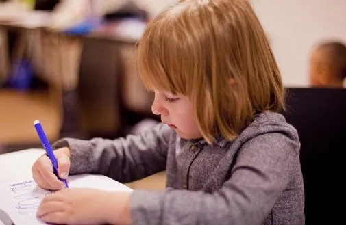 A young child writing sitting at a desk
