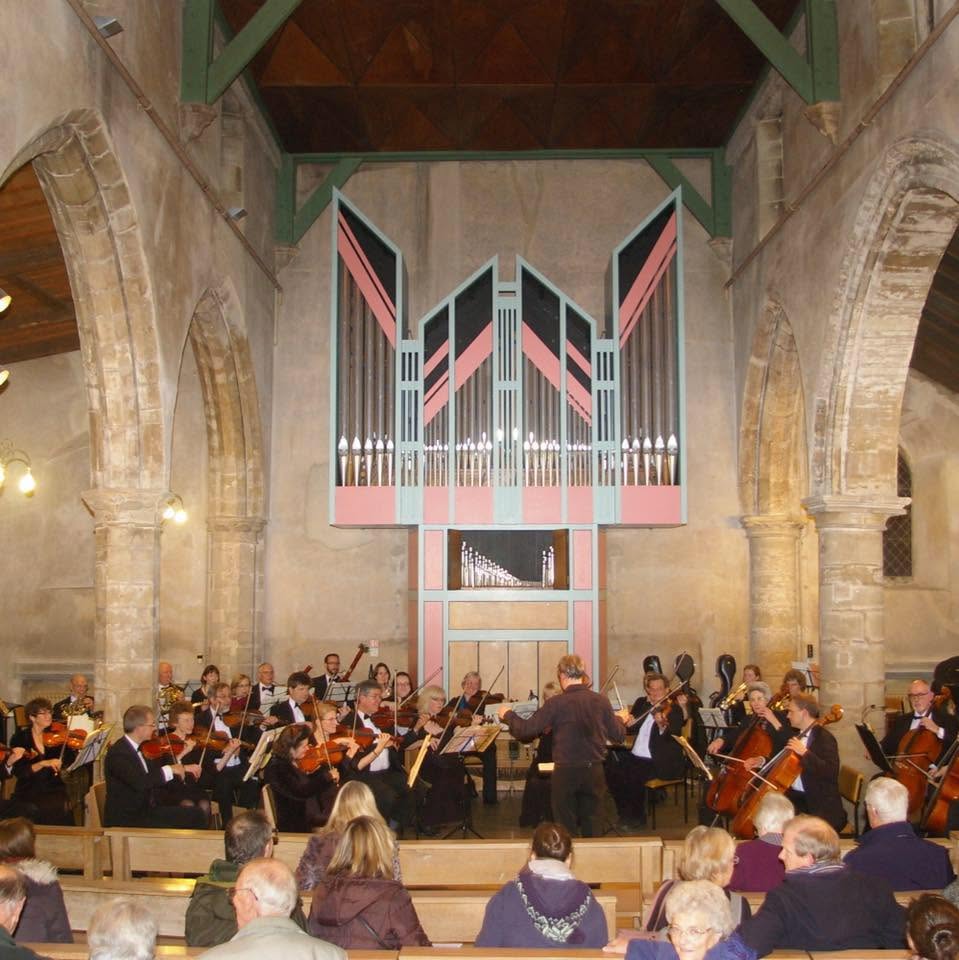 Orchestra performing in a church with an audience seated in pews and a large pipe organ at the front.