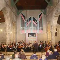 Orchestra performing in a church with an audience seated in pews and a large pipe organ at the front.