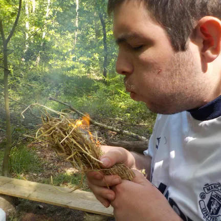 Young man blowing kindling to make fire