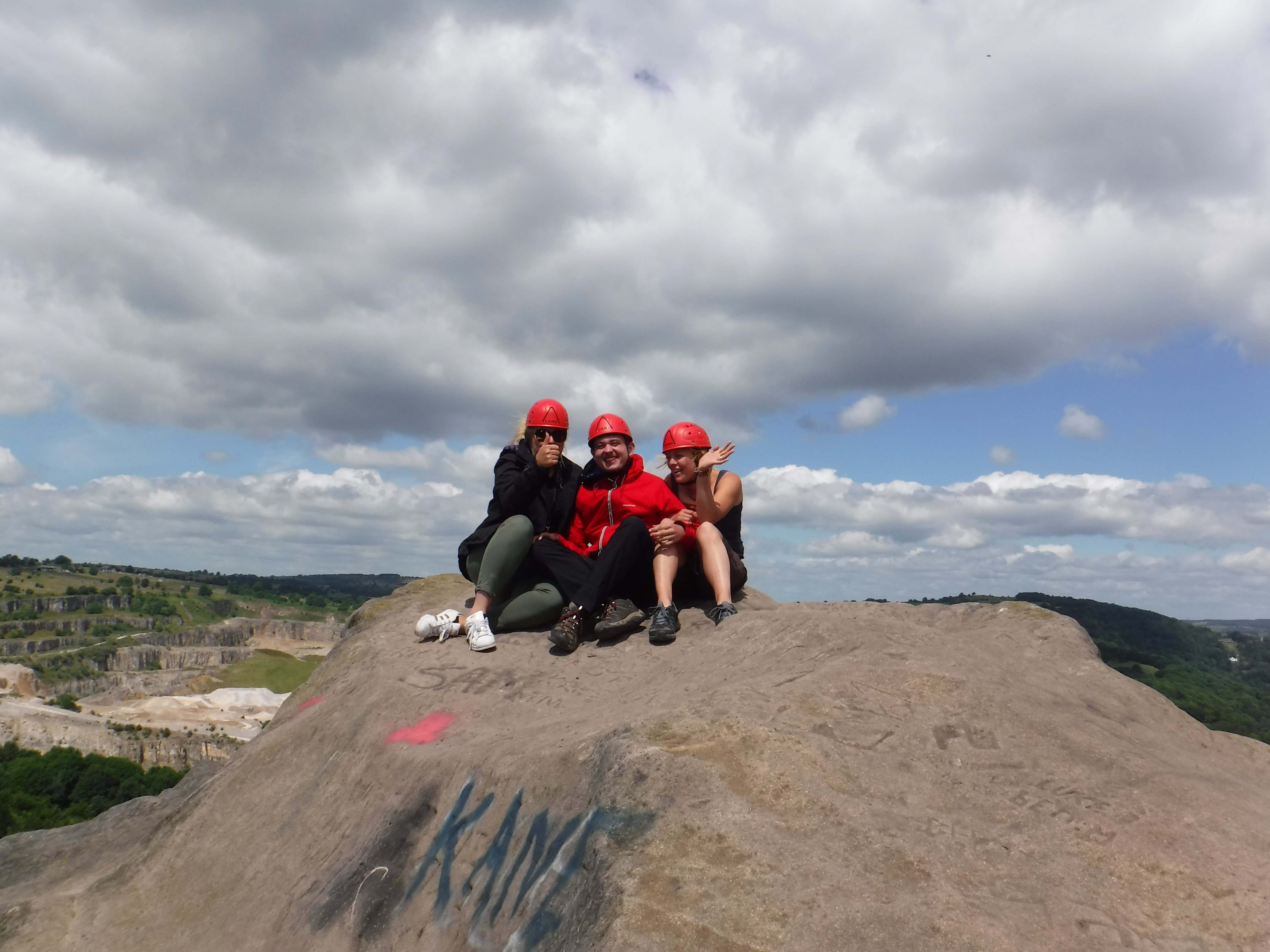 Group of young people with red climbing helmets sat on a rock