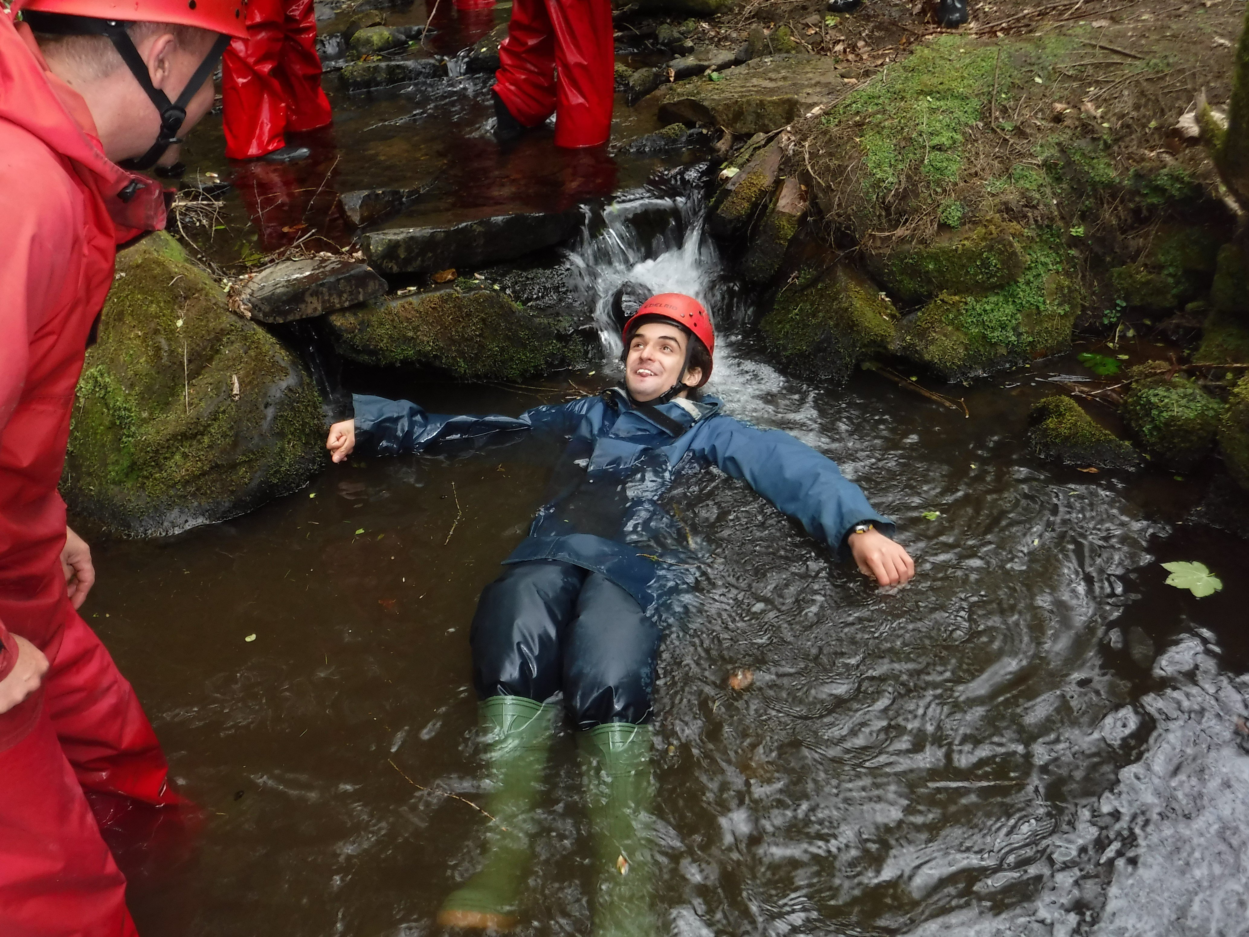 Man in caving equipment lying in a stream