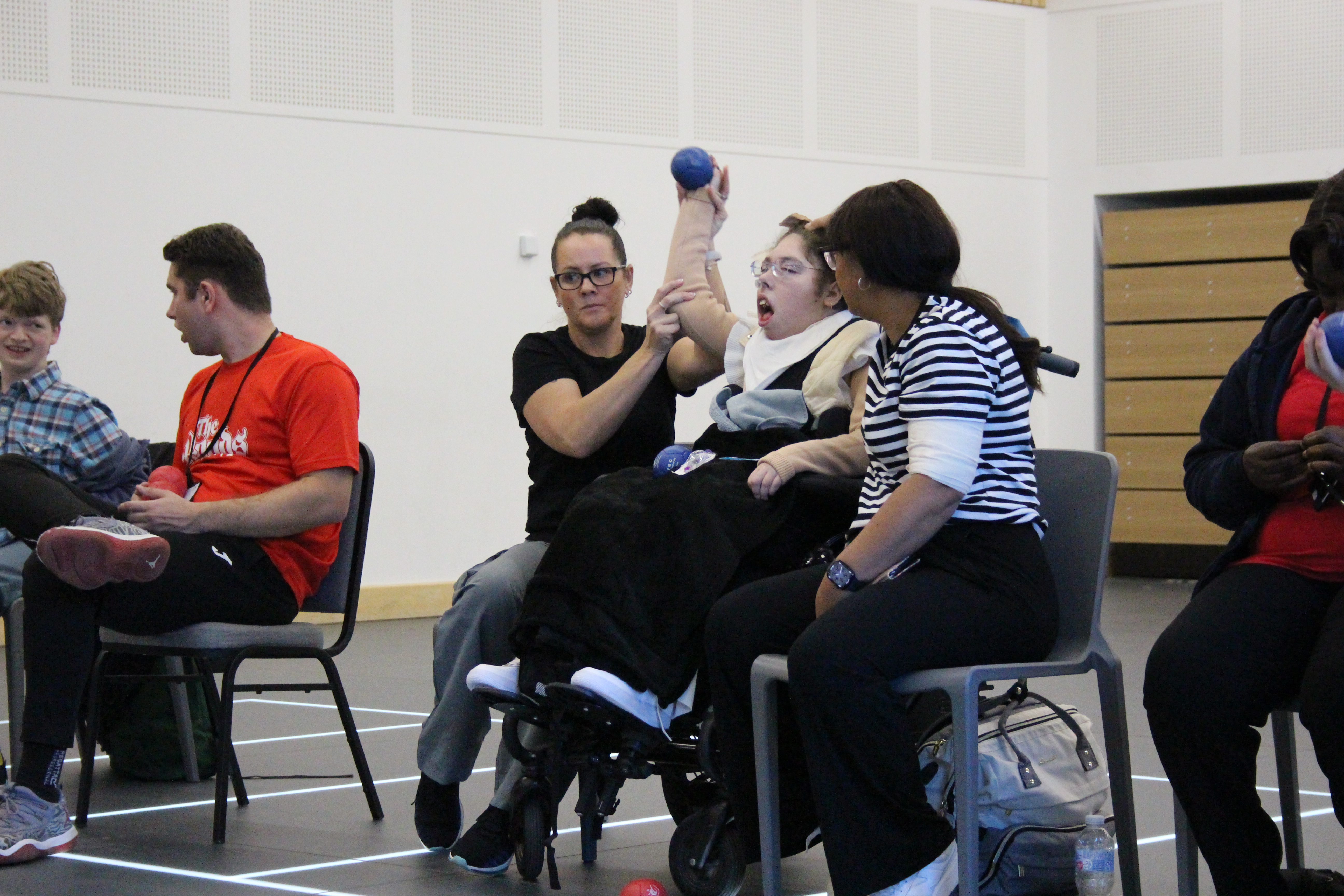 Image of a young lady in a wheelchair playing boccia with carers