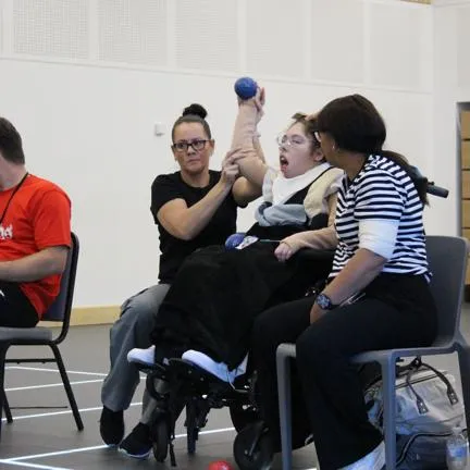 Image of a young lady in a wheelchair playing boccia with carers