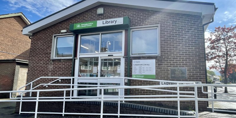 Front view of Ladybrook library entrance, red brick building with an accessibility ramp leading to glass double doors.