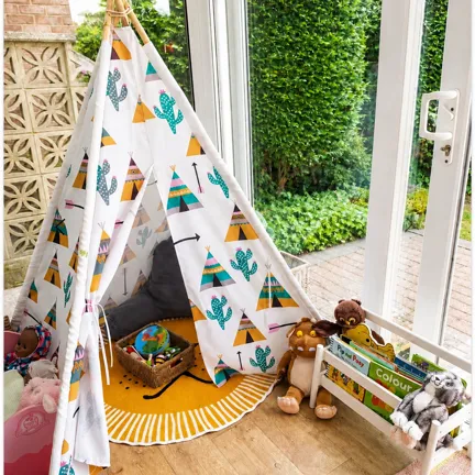 Children’s play area with a patterned teepee tent, round rug, plush toys, and a toy storage rack by large windows.